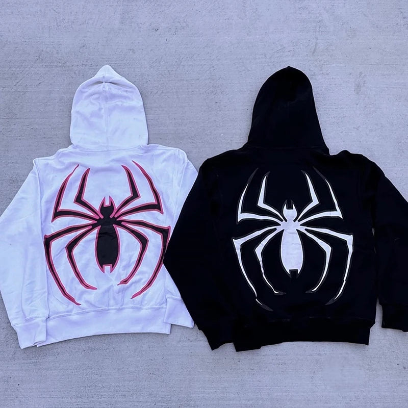 Two hoodies, one white and one black, with spider logos on a gray surface.